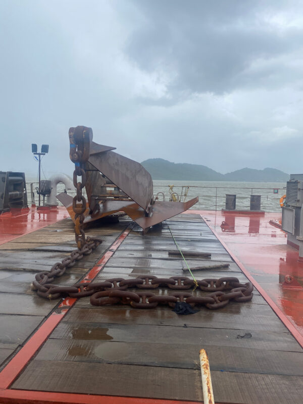 An anchor coming down onto a wet deck, the sea and hills behind