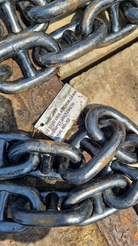 A works tag wired to a shot of stud link anchor chain reading: U2 STUD LINK ANCHOR CHAIN, 22MM x 27.5M/LENGTH, SERIAL NO. 52