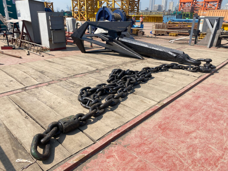 A stockless bower anchor with its chain ranged along a barge deck, yard cranes behind